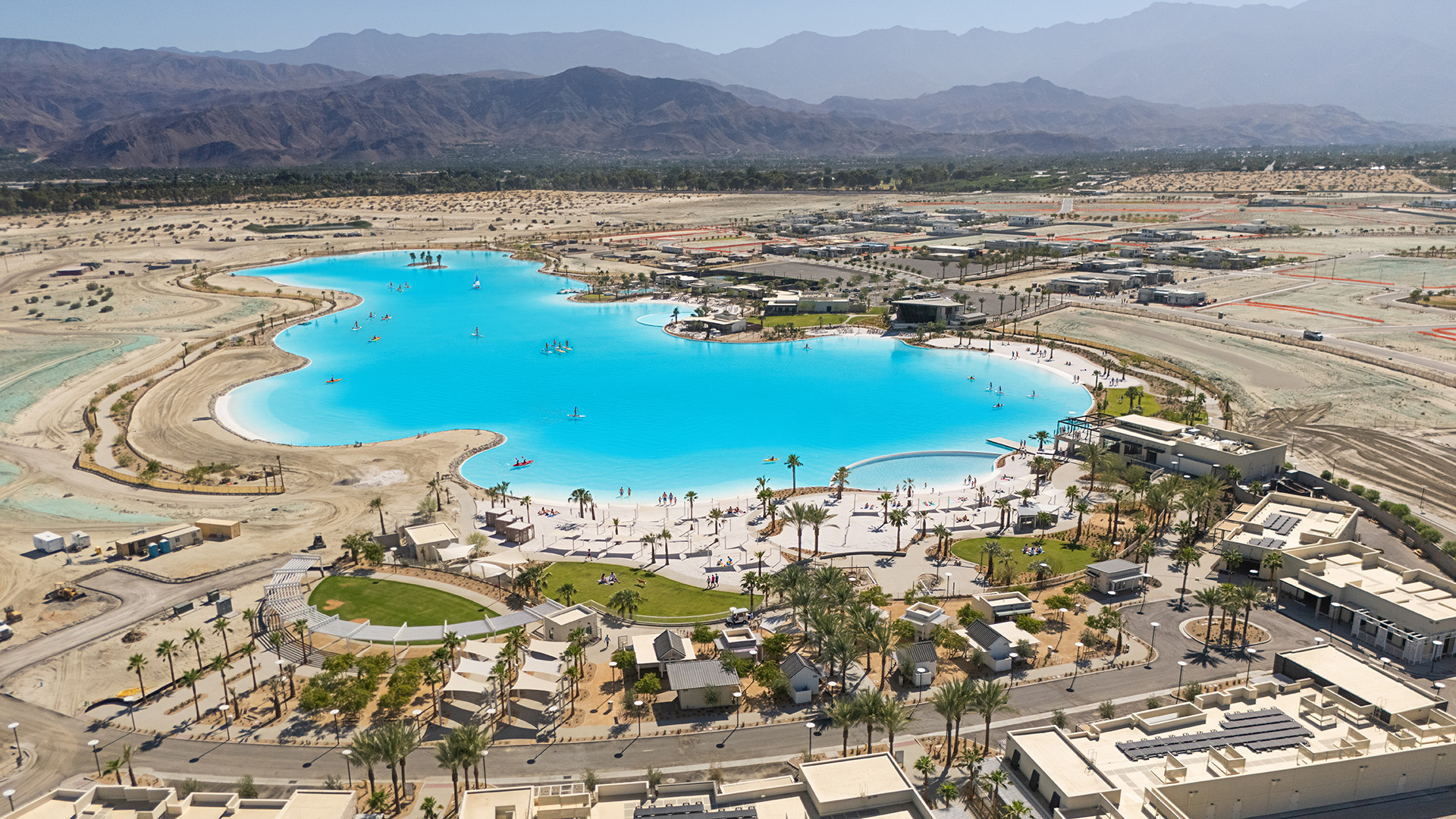 Aerial view of the Cotino lagoon shoreline at Cotino Bay, Crystal Lagoons lagoon in Rancho Mirage, California, with the Artisan Club and mountains in the background
